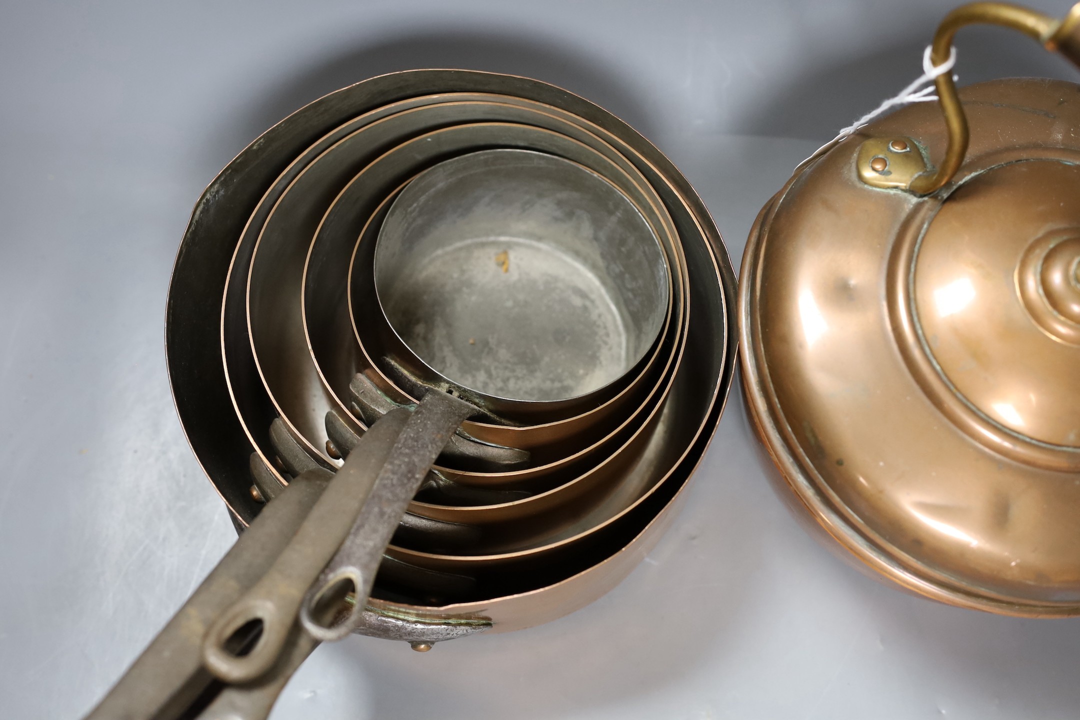 A group of graduated copper pans together with a brass kettle